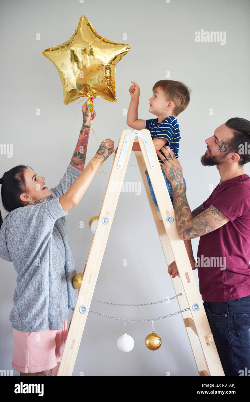 Modern family decorating the home at Christmas time using ladder as Christmas tree Stock Photo