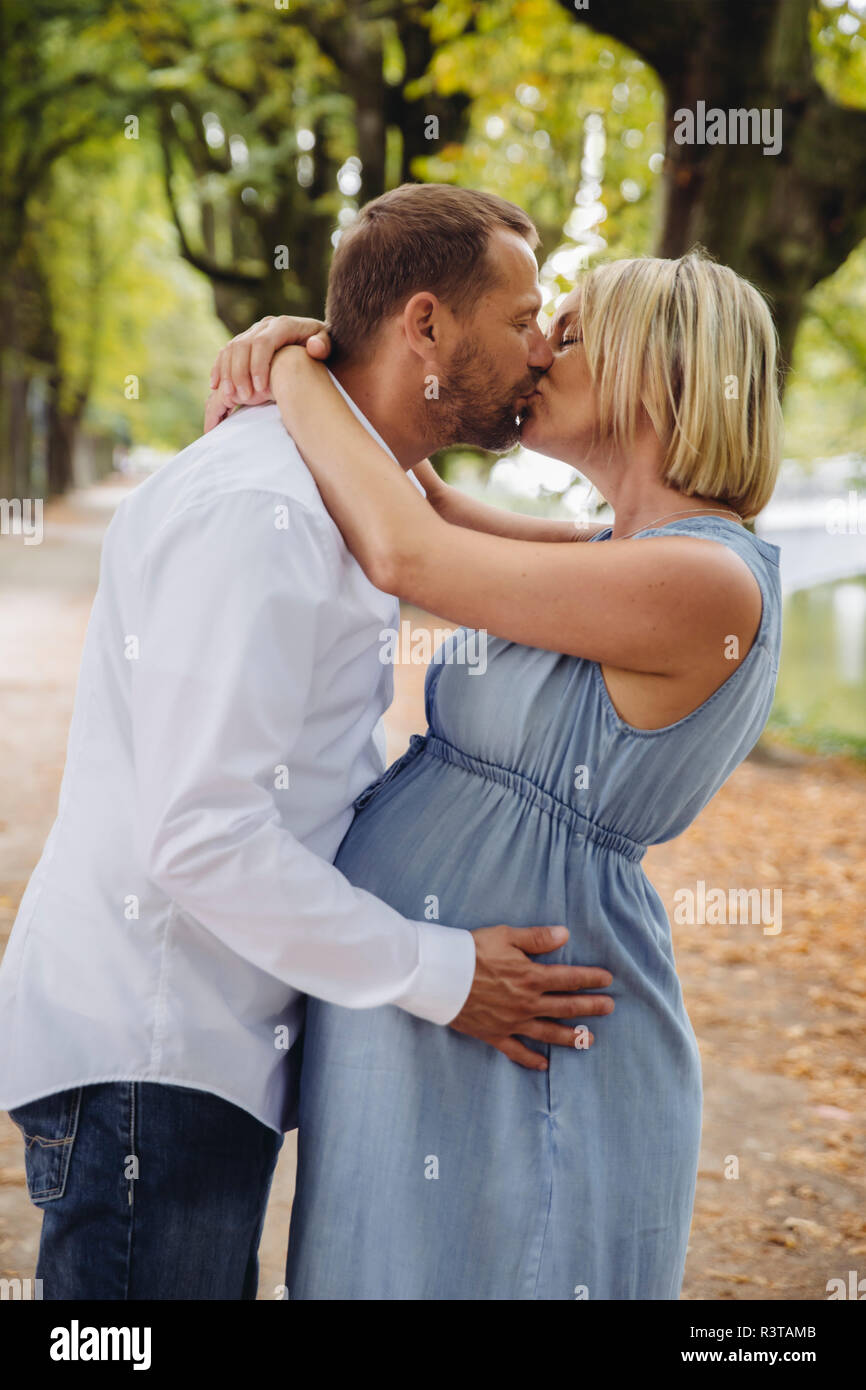 Mature pregnant couple kissing in park Stock Photo
