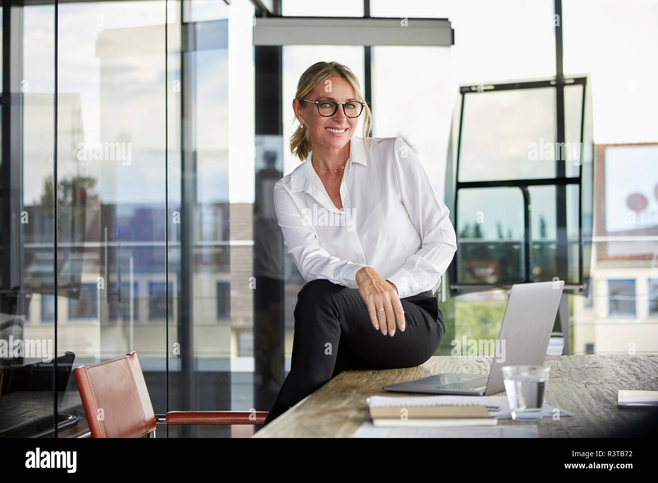 Businesswoman sitting on desk, smiling friendly Stock Photo