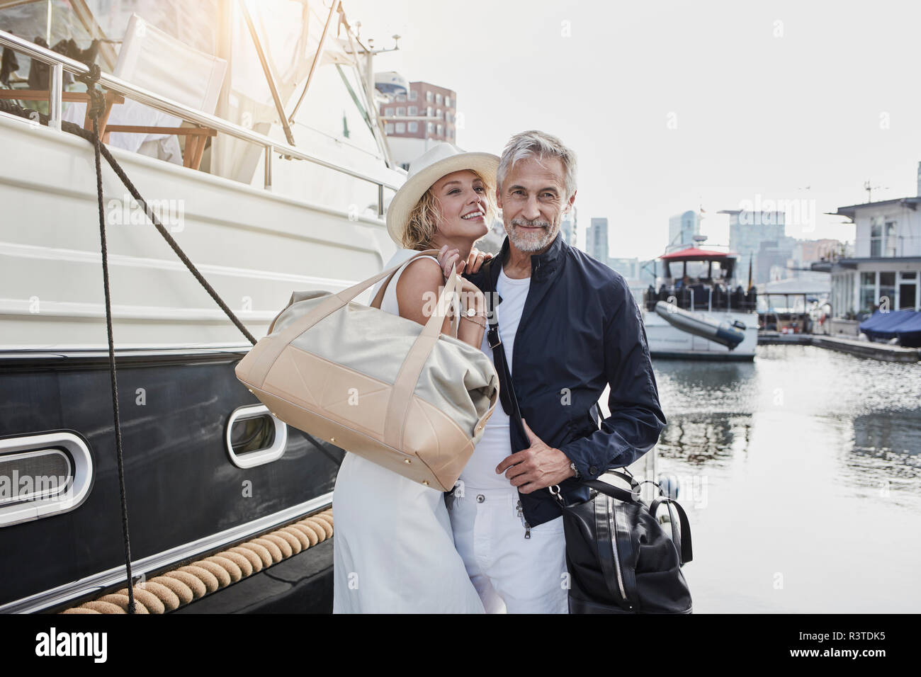 Older man and young woman standing with travelling bags on jetty next to yacht Stock Photo