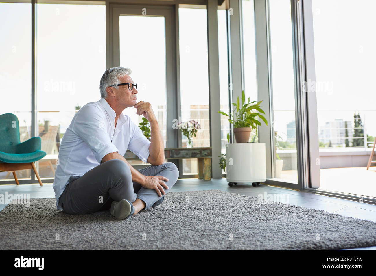 Pensive mature man sitting on carpet at home Stock Photo