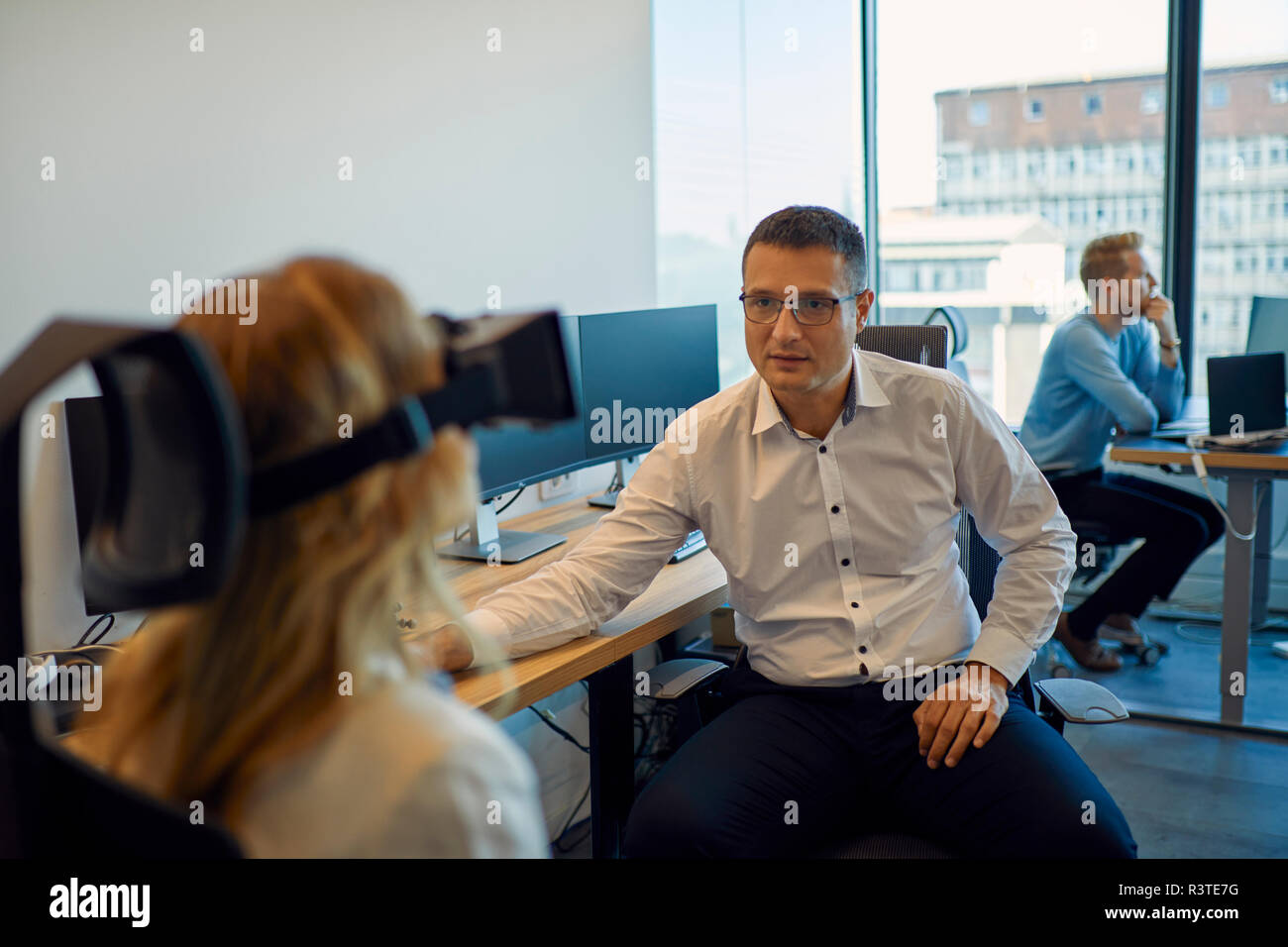 Man looking at woman wearing VR glasses in office Stock Photo - Alamy