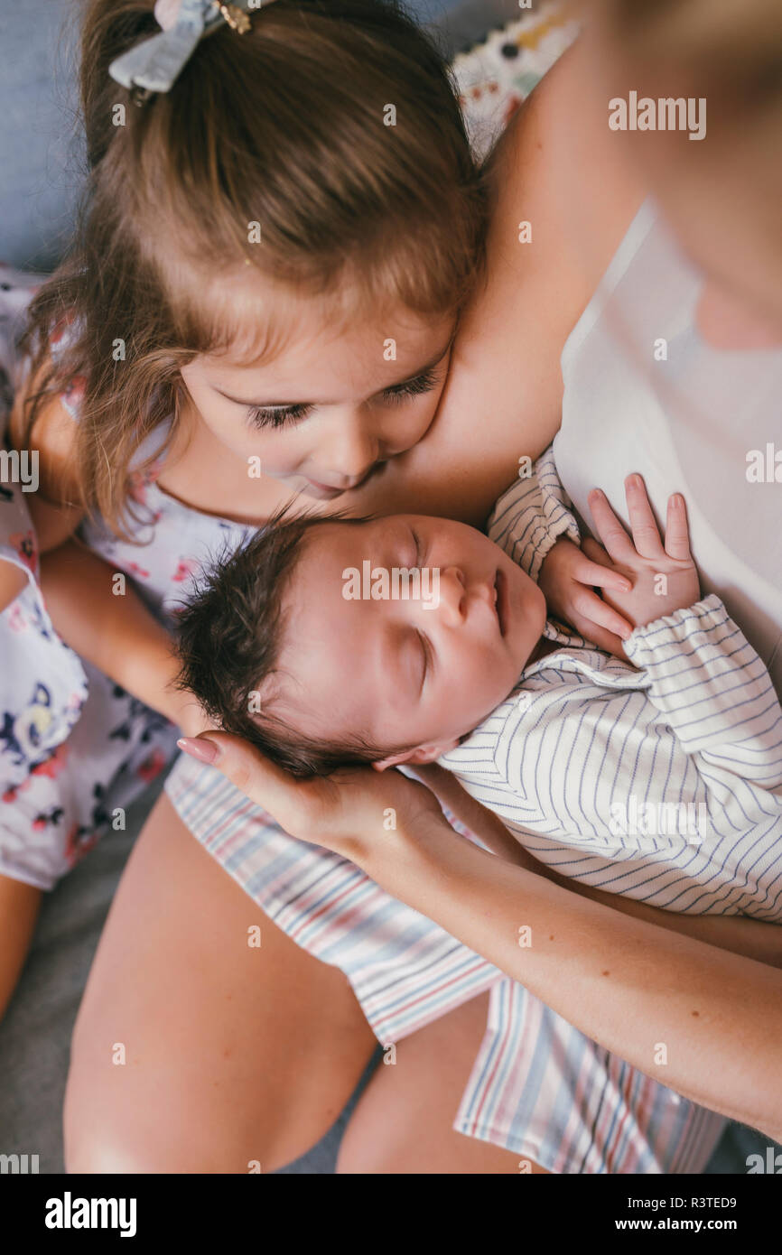 Mother holding her baby close with sister looking at him Stock Photo