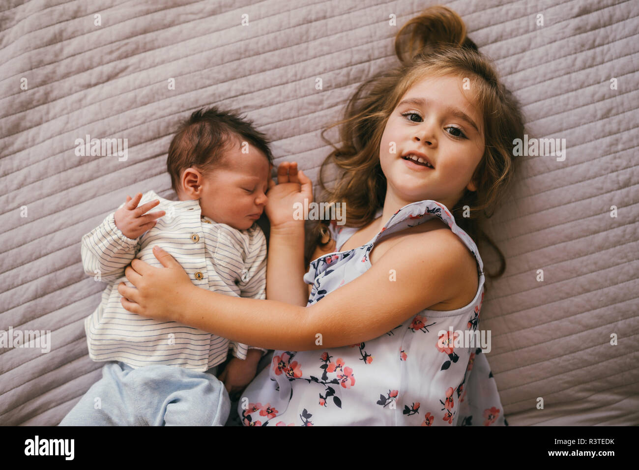 Smiling girl lying on blanket cuddling with her baby brother Stock Photo