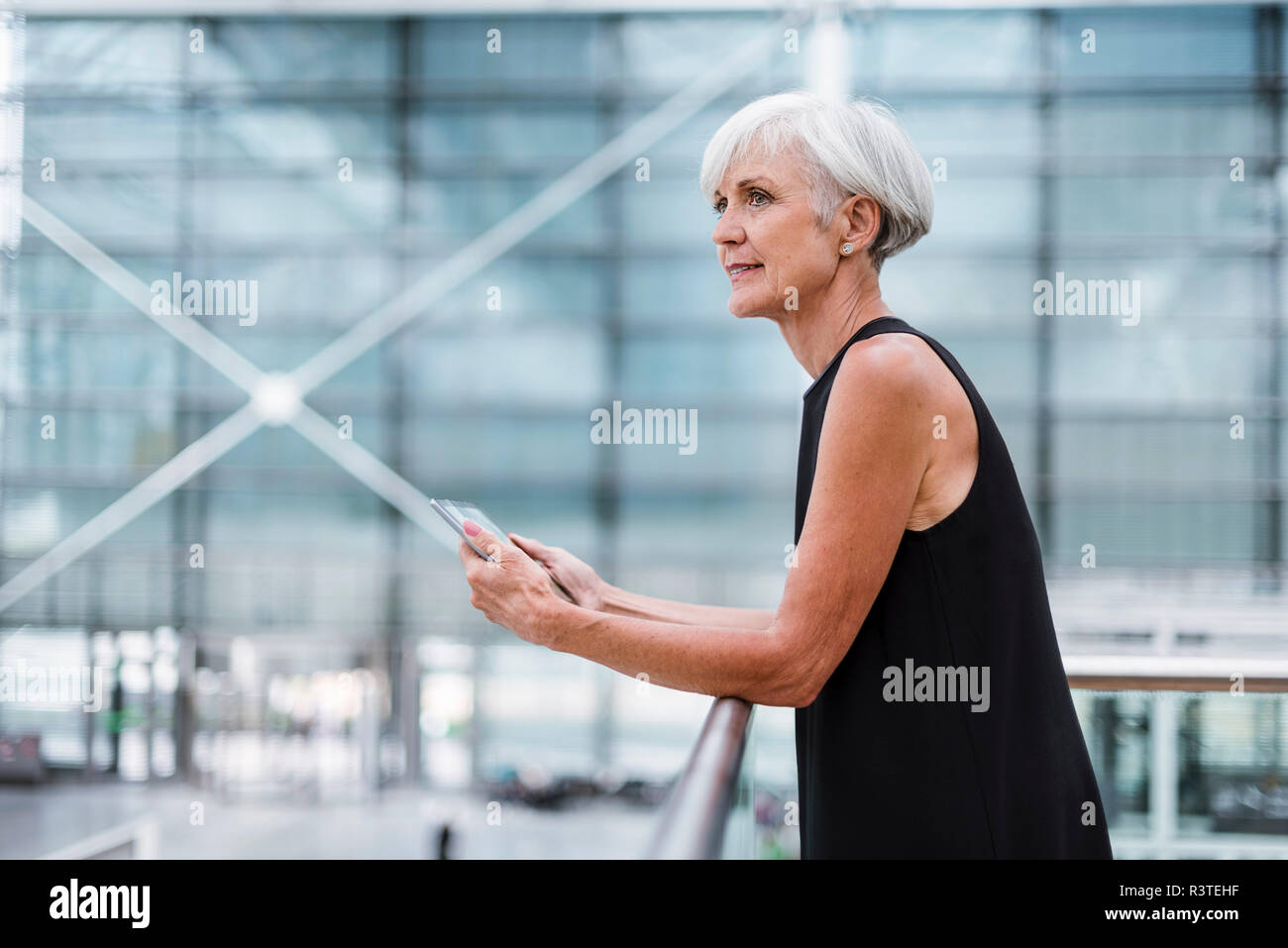Senior woman with tablet wearing black dress leaning against a railing Stock Photo