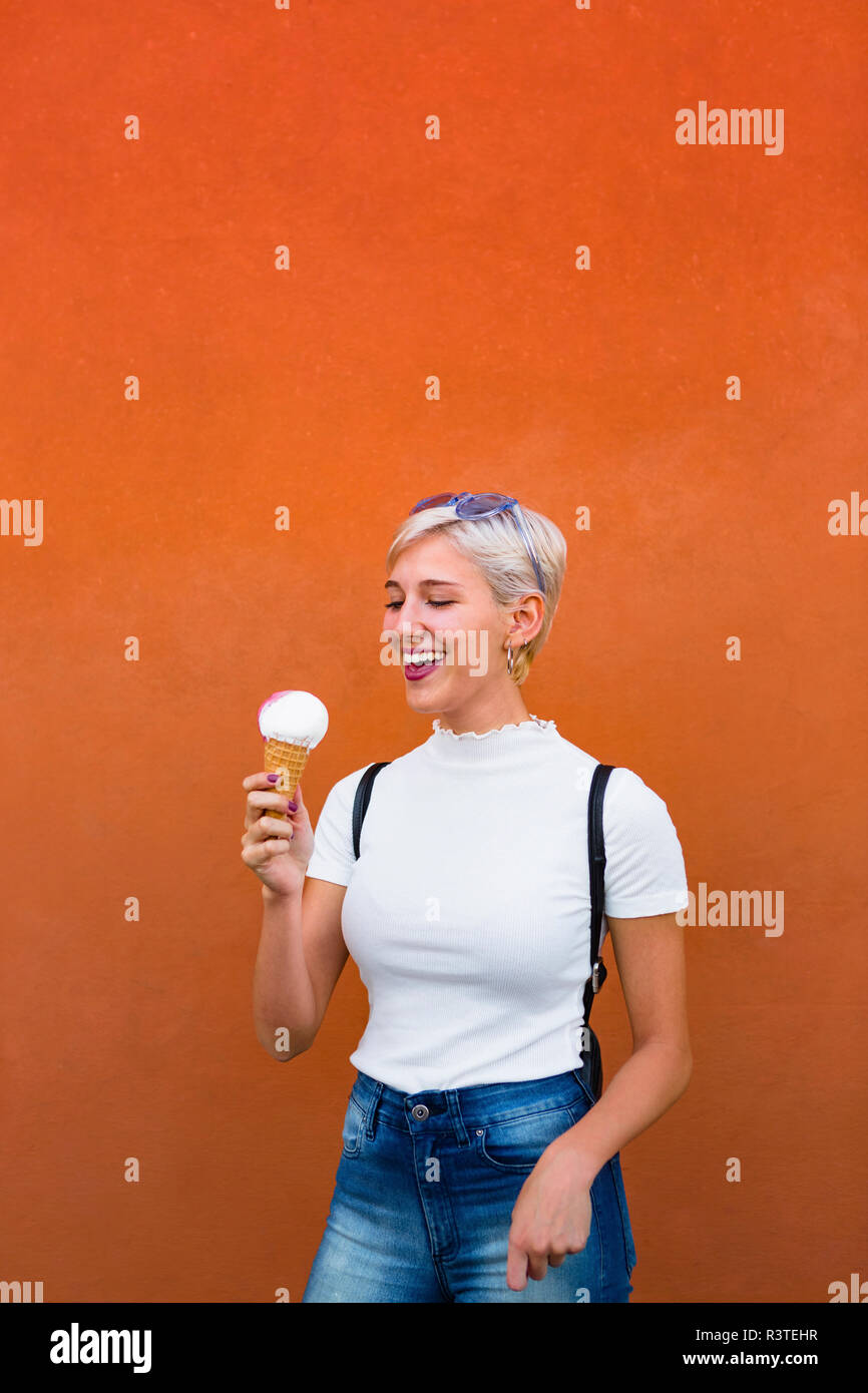 Laughing young woman with ice cream cone in front of orange background Stock Photo