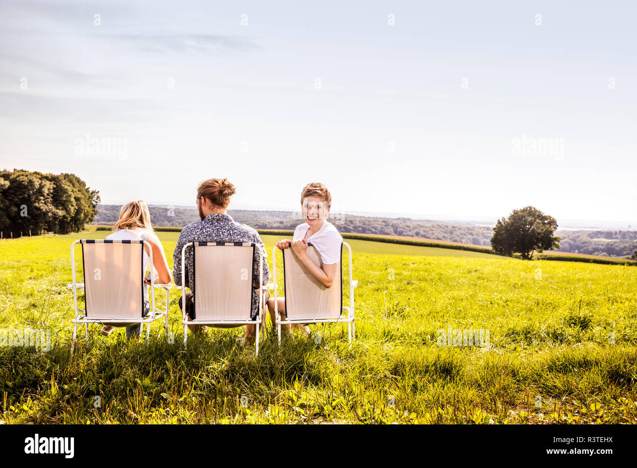 Friends sitting on camping chairs in rural landscape Stock Photo