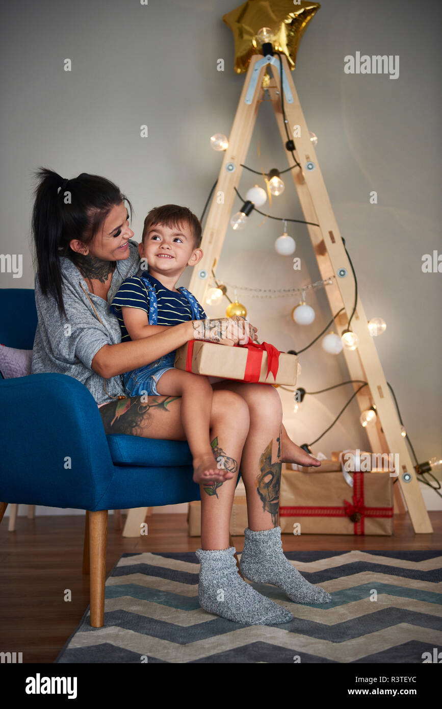 Happy boy opening Christmas present with his mother at home Stock Photo