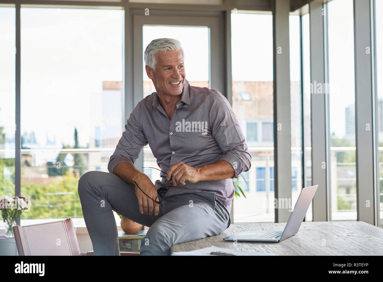 Smiling mature man with laptop sitting on table at home Stock Photo