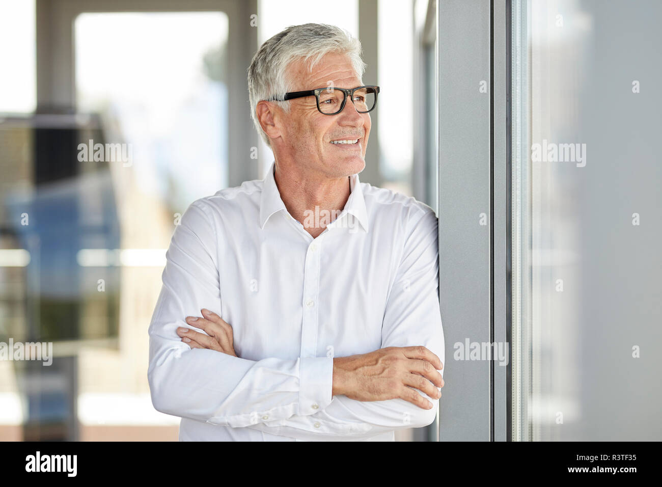 Businessman in office leaning against window, with arms crossed Stock Photo