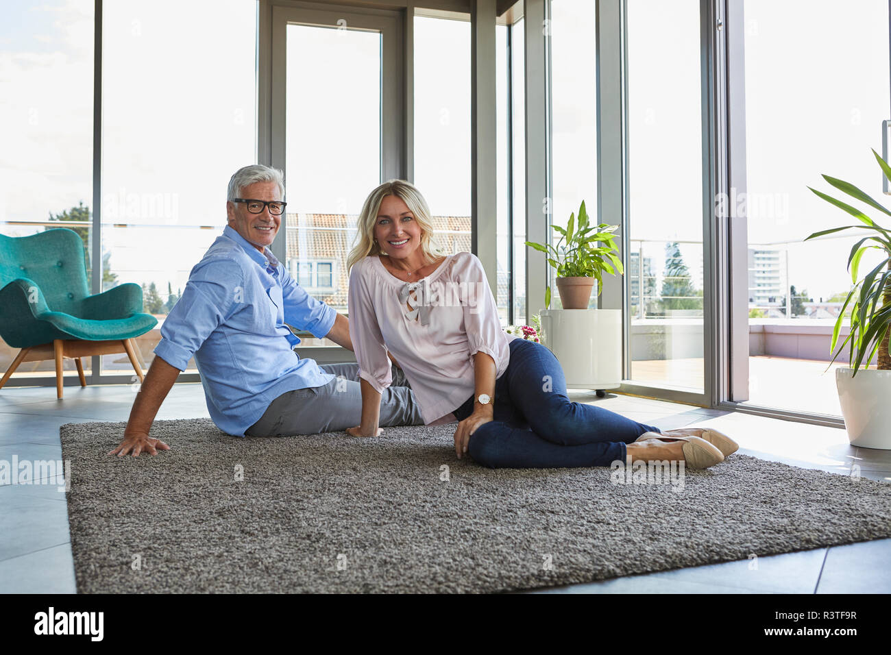 Portrait of smiling mature couple relaxing at home sitting on carpet Stock Photo