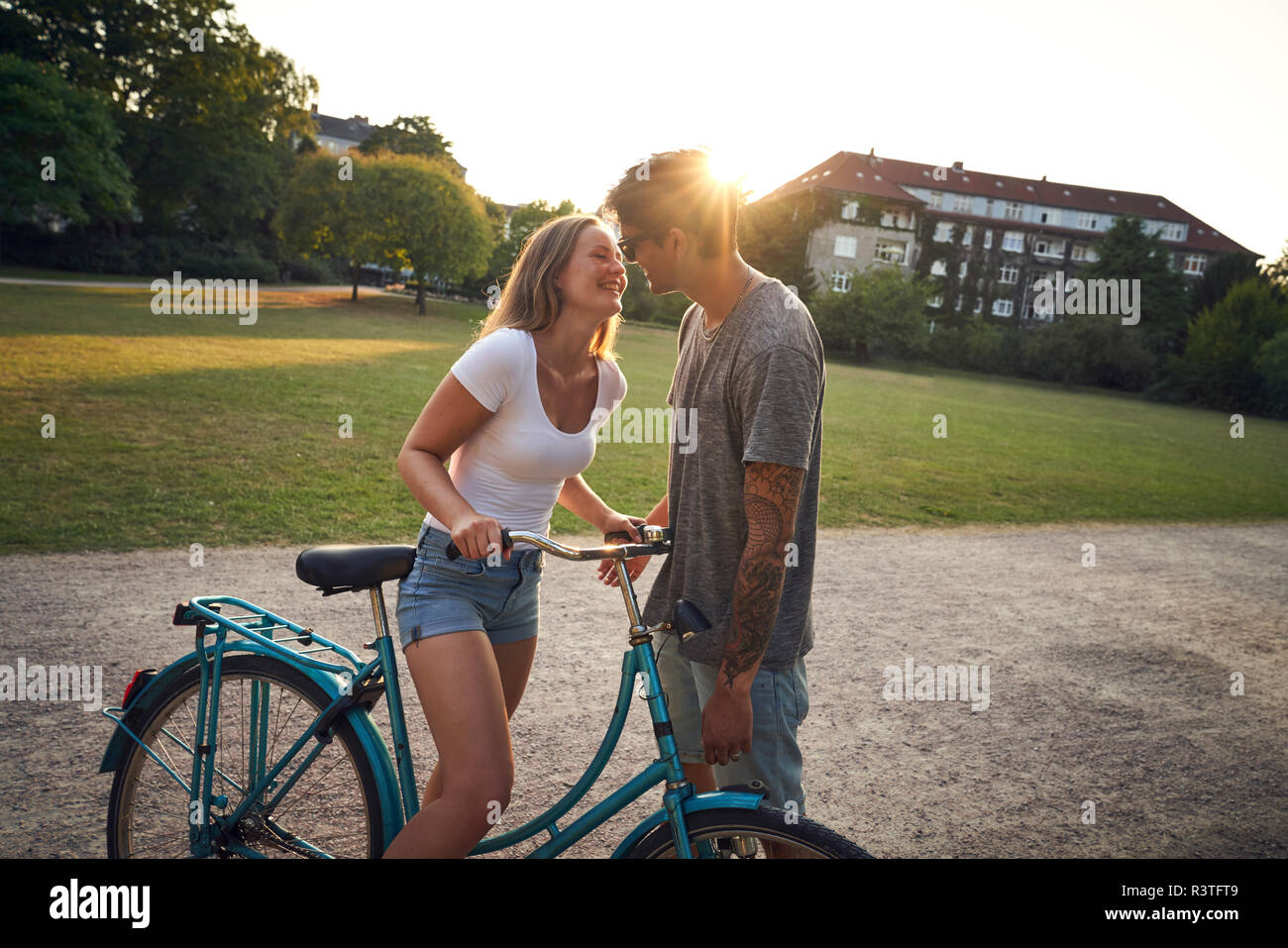 Young woman with bicycle, kissing her boyfriend in park Stock Photo