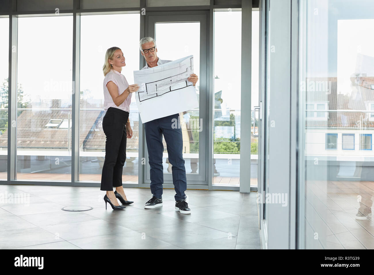 Businessman and woman standing in office, discussing blueprint Stock Photo
