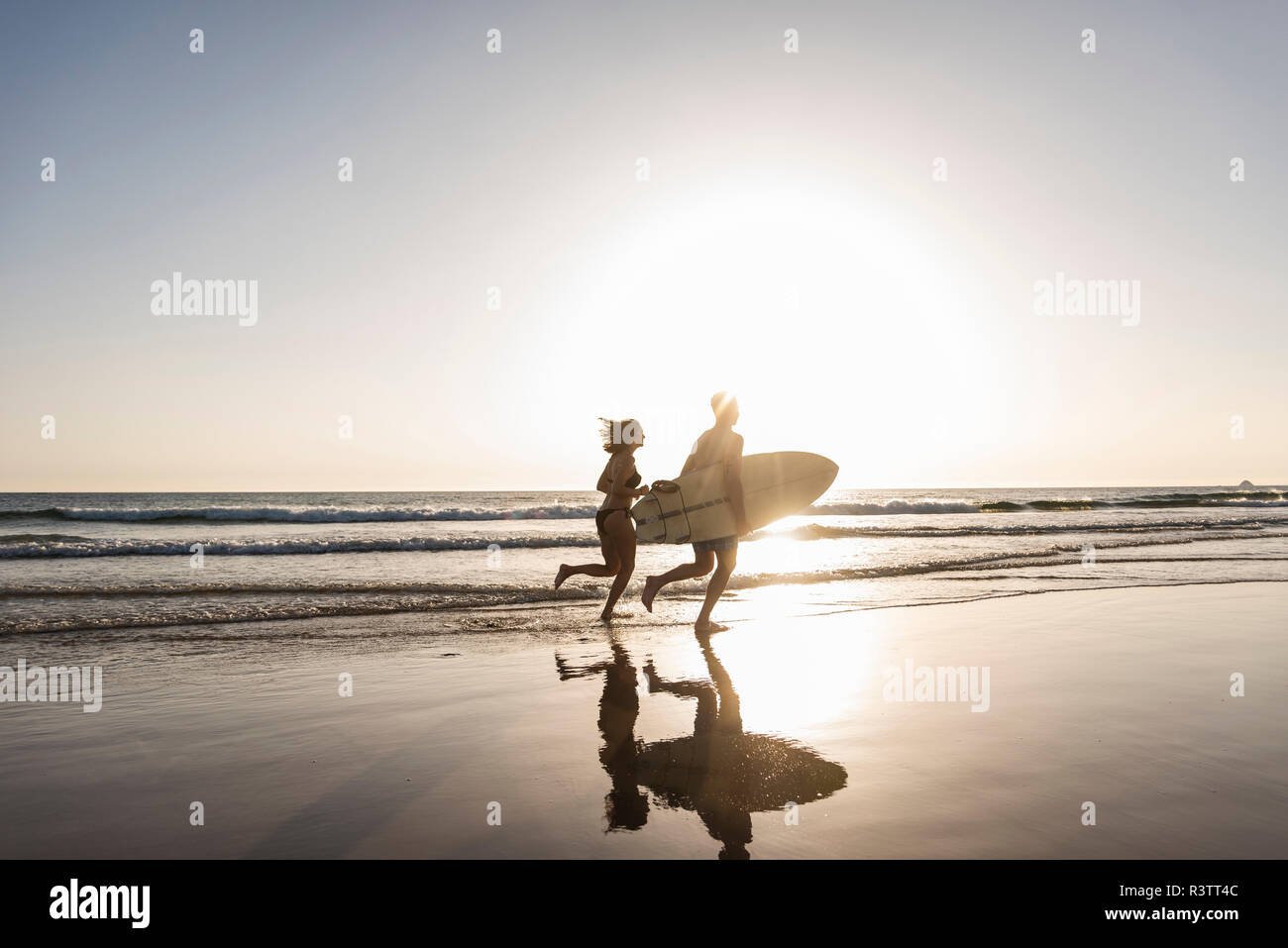 Young couple running on beach, carrying surfboard Stock Photo