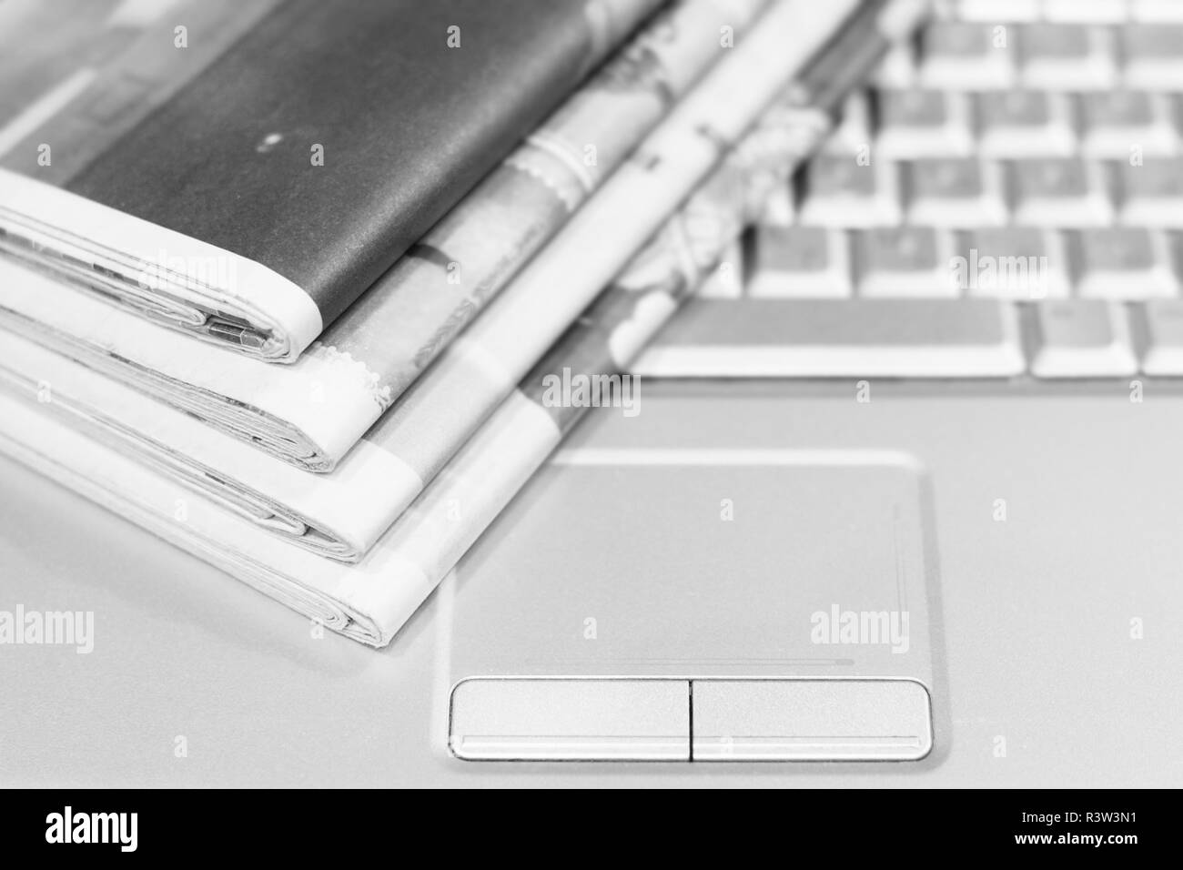 Newspaper and laptop. Pile of daily papers with news on the computer. Pages with headlines, articles folded and stacked on keypad of electronic device Stock Photo