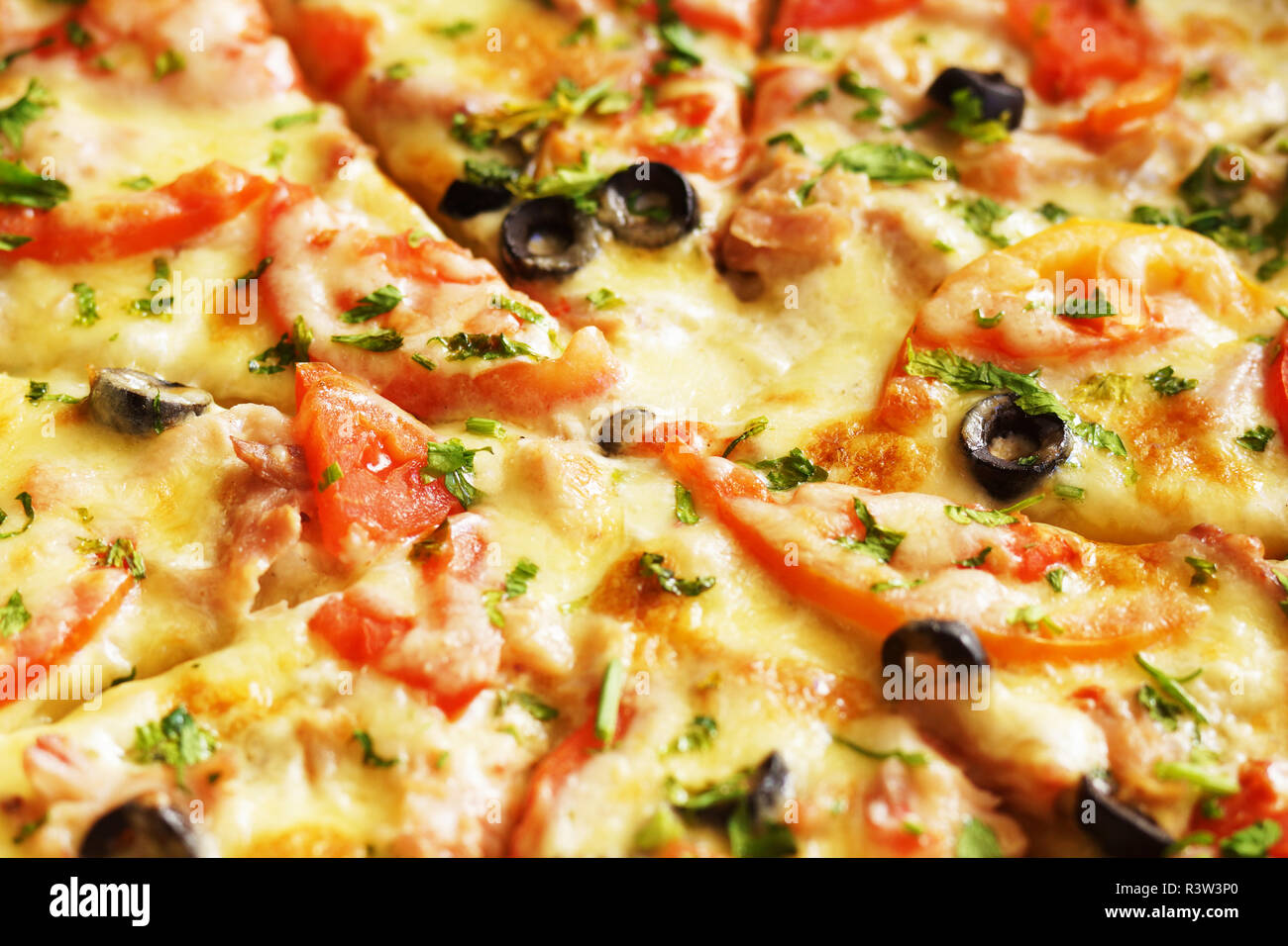 Hot pizza with cheese, ham and chicken, fresh tomato slices and olives cutted to pieces. Could be used as food background or in restaurant menu Stock Photo