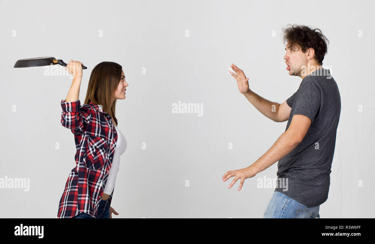 Woman with cooking pan being angry at her man. Couple standing against white background Stock Photo