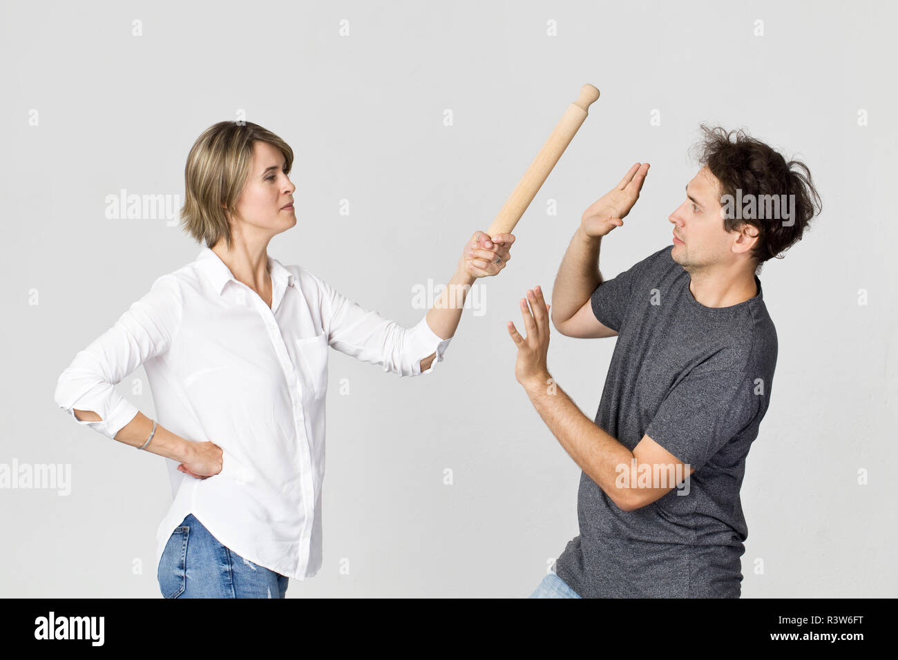 Woman hitting man with rolling pin. Family scene against white