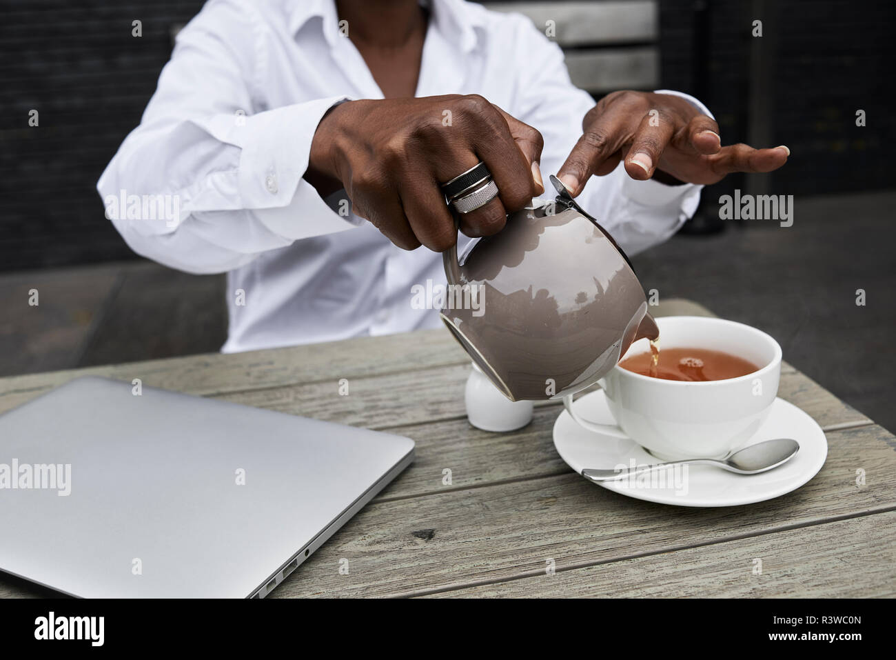 Hands of businesswoman sitting on  terrace of a coffee shop pouring tea into a cup Stock Photo