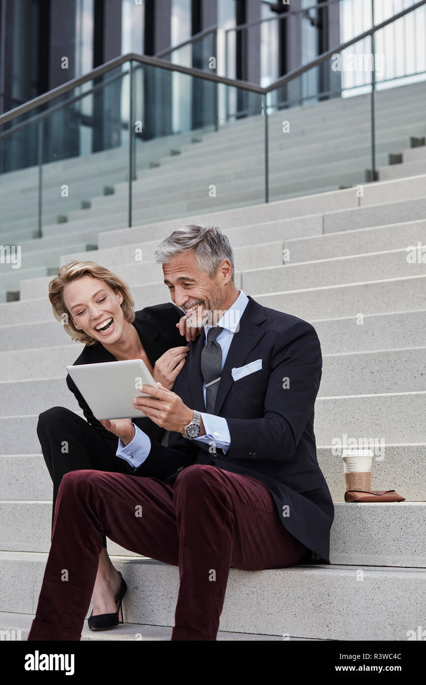 Portrait of two businesspeople sitting together on stairs looking at tablet having fun Stock Photo