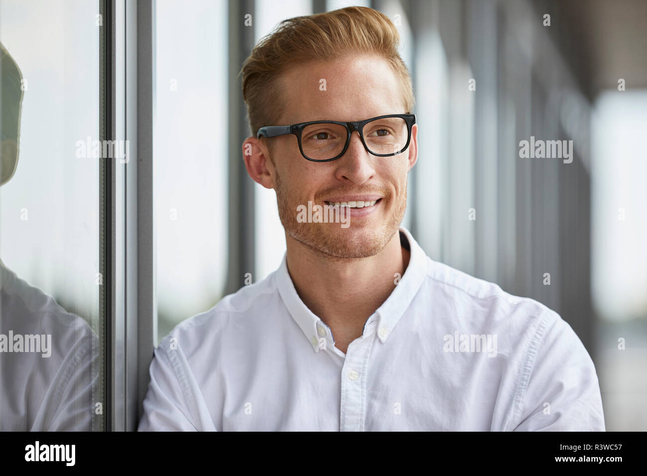 Portrait of smiling businessman leaning against window Stock Photo