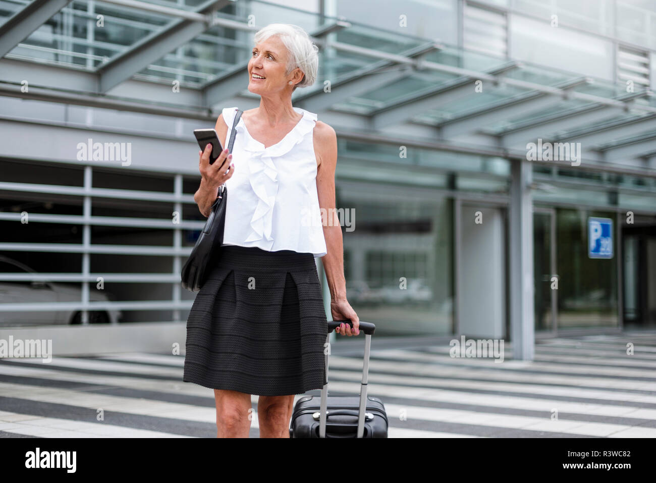 Smiling senior woman with cell phone and baggage on the move Stock Photo