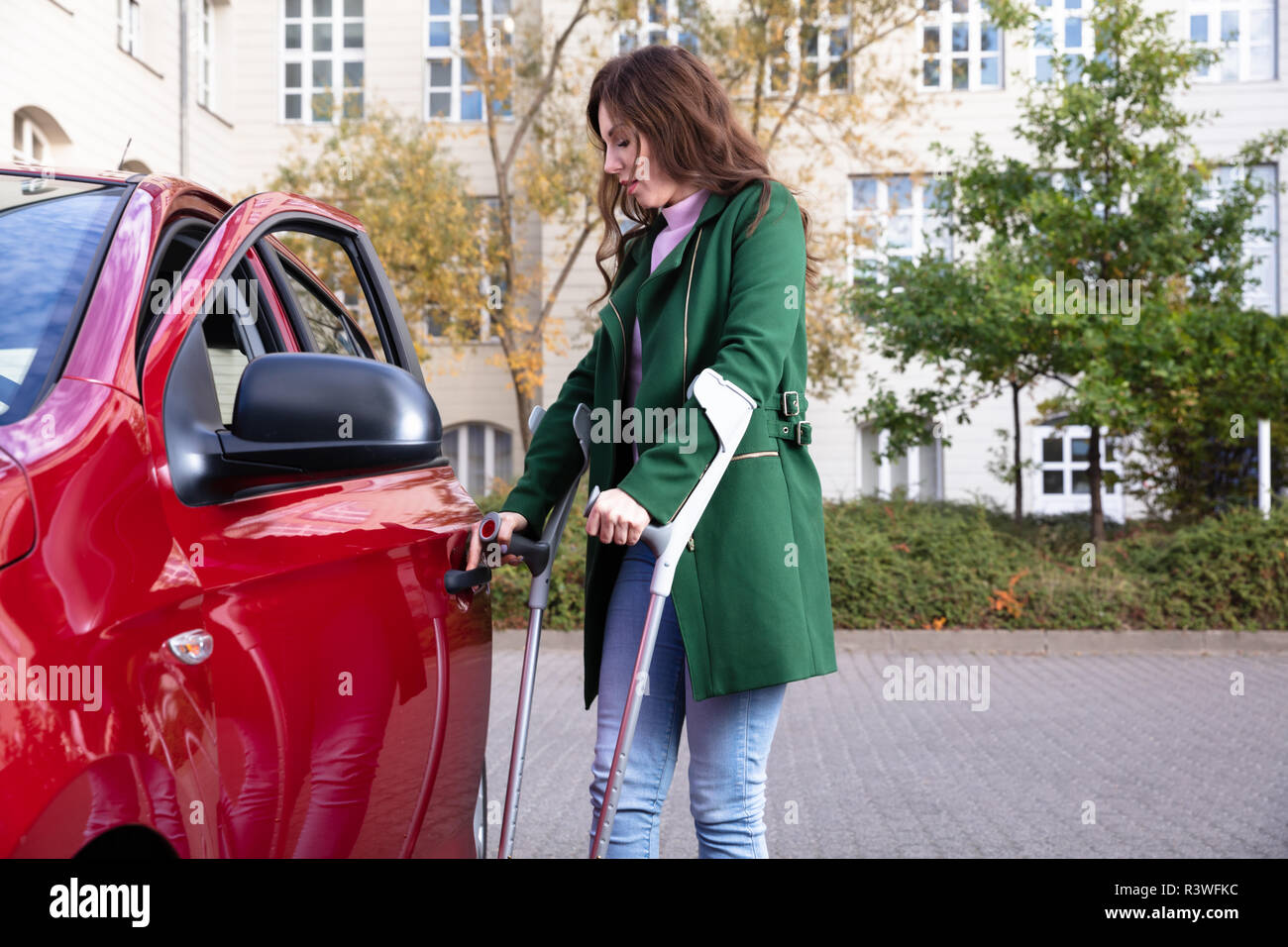 Disabled Young Woman With Crutches Opening Door Of A Red Car Stock Photo