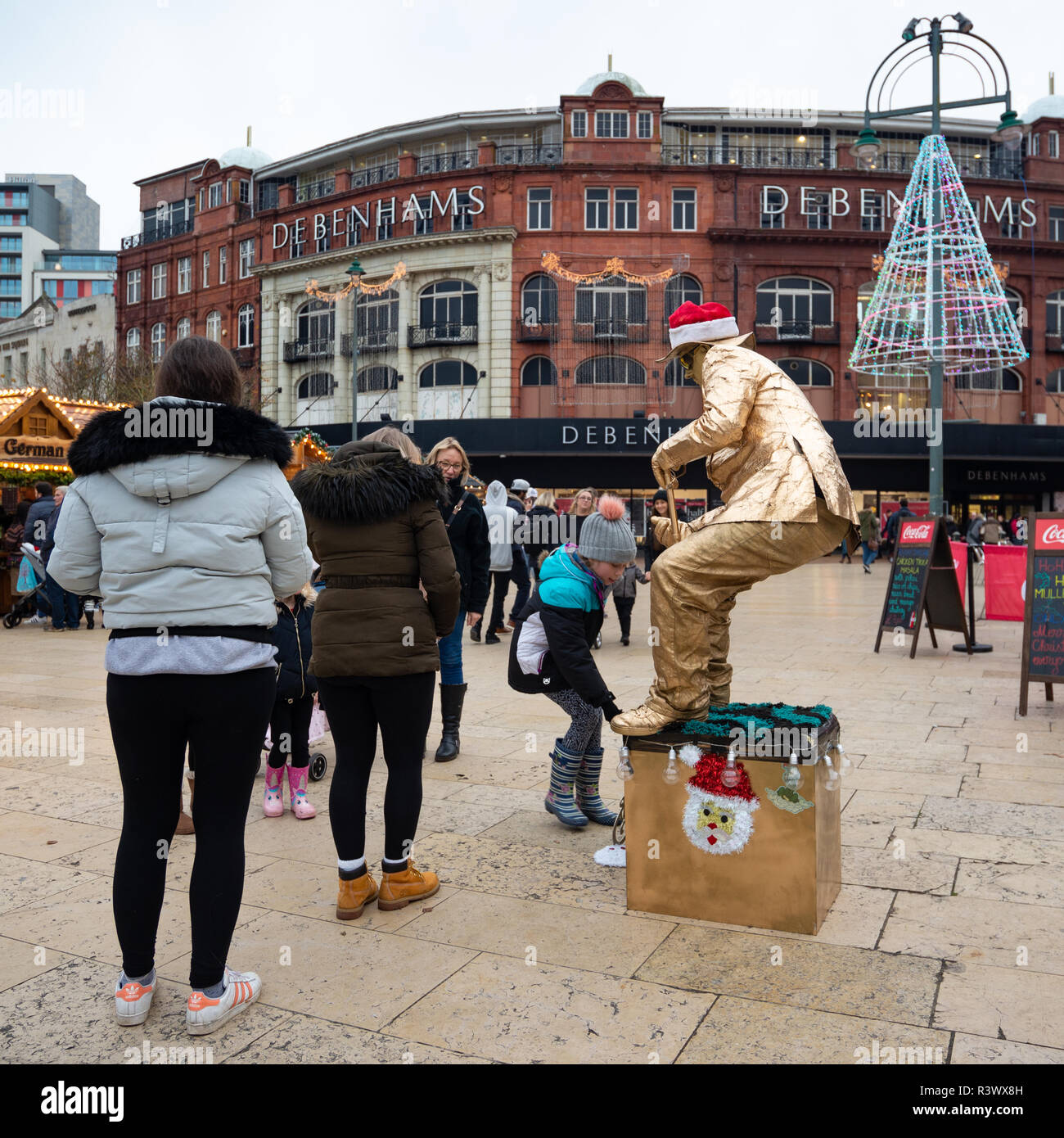 Festive Christmas scene with a gold painted sitting live statue entertaining families in The Square, Bournemouth, Dorset, UK Stock Photo
