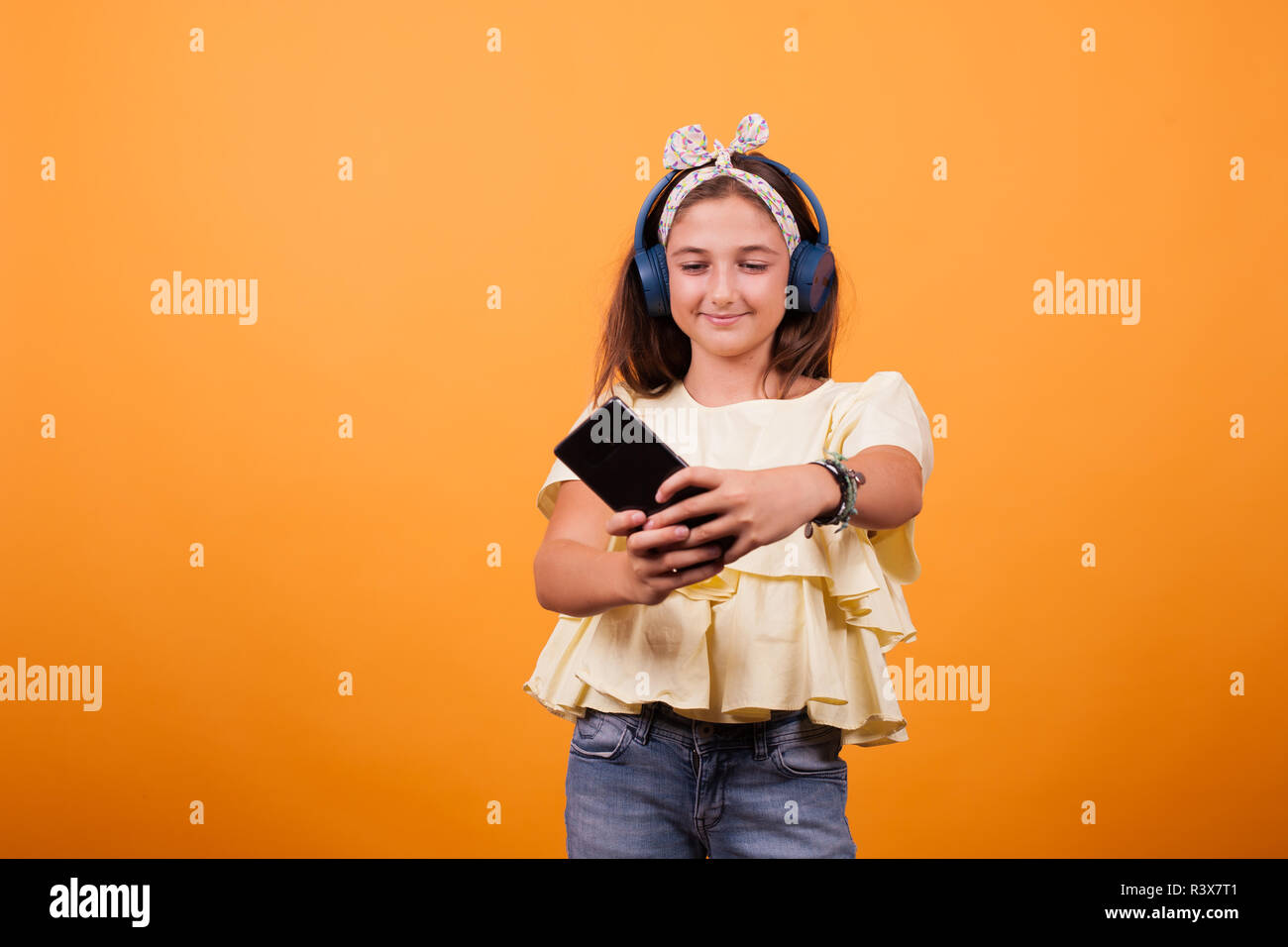 Little girl with yellow t-shirt listening music from her phone and headset. Joyfull gil Stock Photo