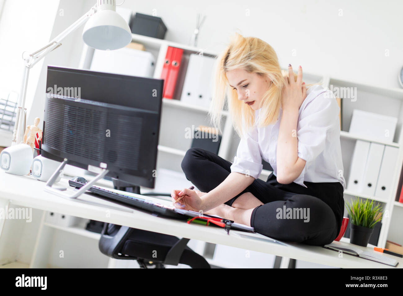 A young girl sitting on a Desk in the office and working with documents and computer. Stock Photo