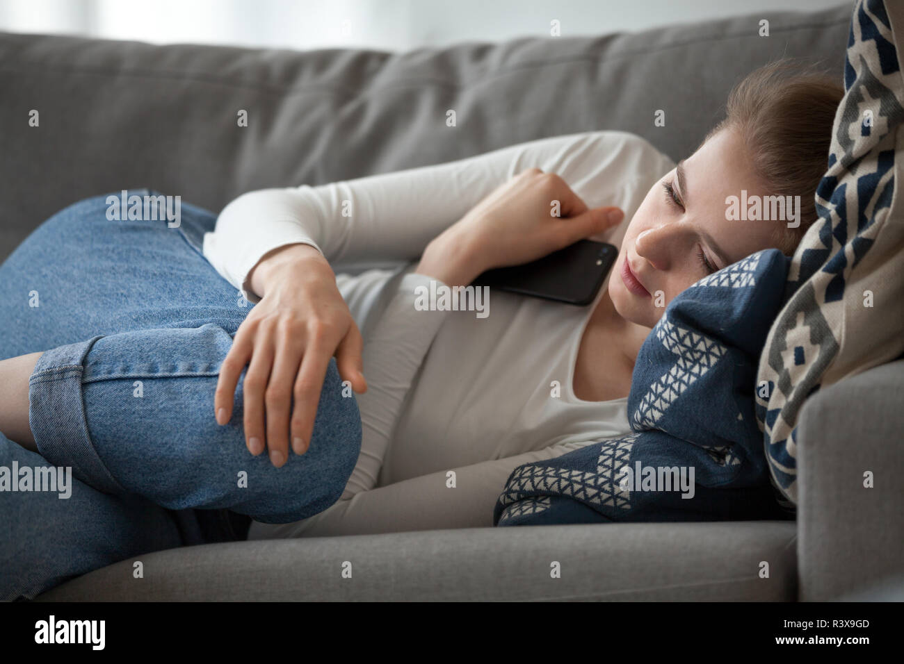 Upset female lying on couch with smartphone in hands Stock Photo