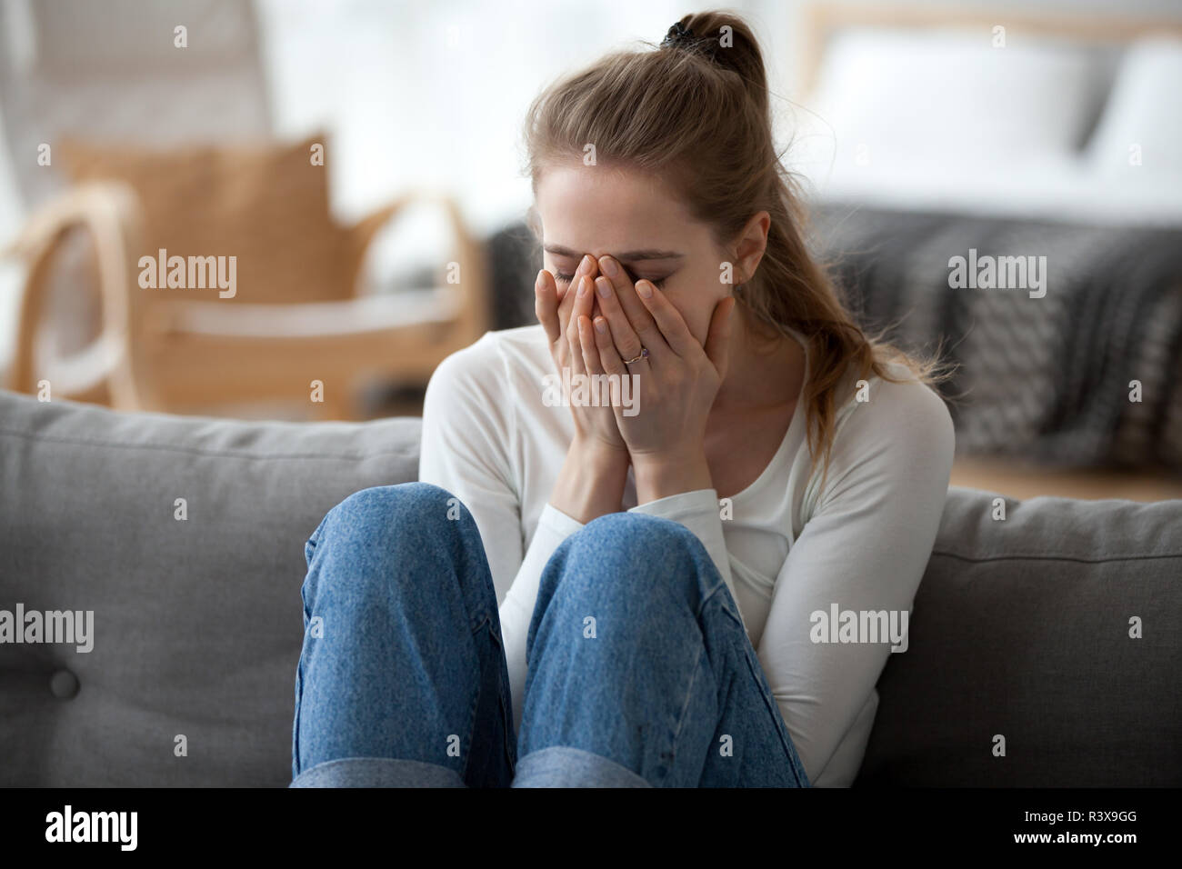 Upset girl sit on sofa crying after breakup Stock Photo