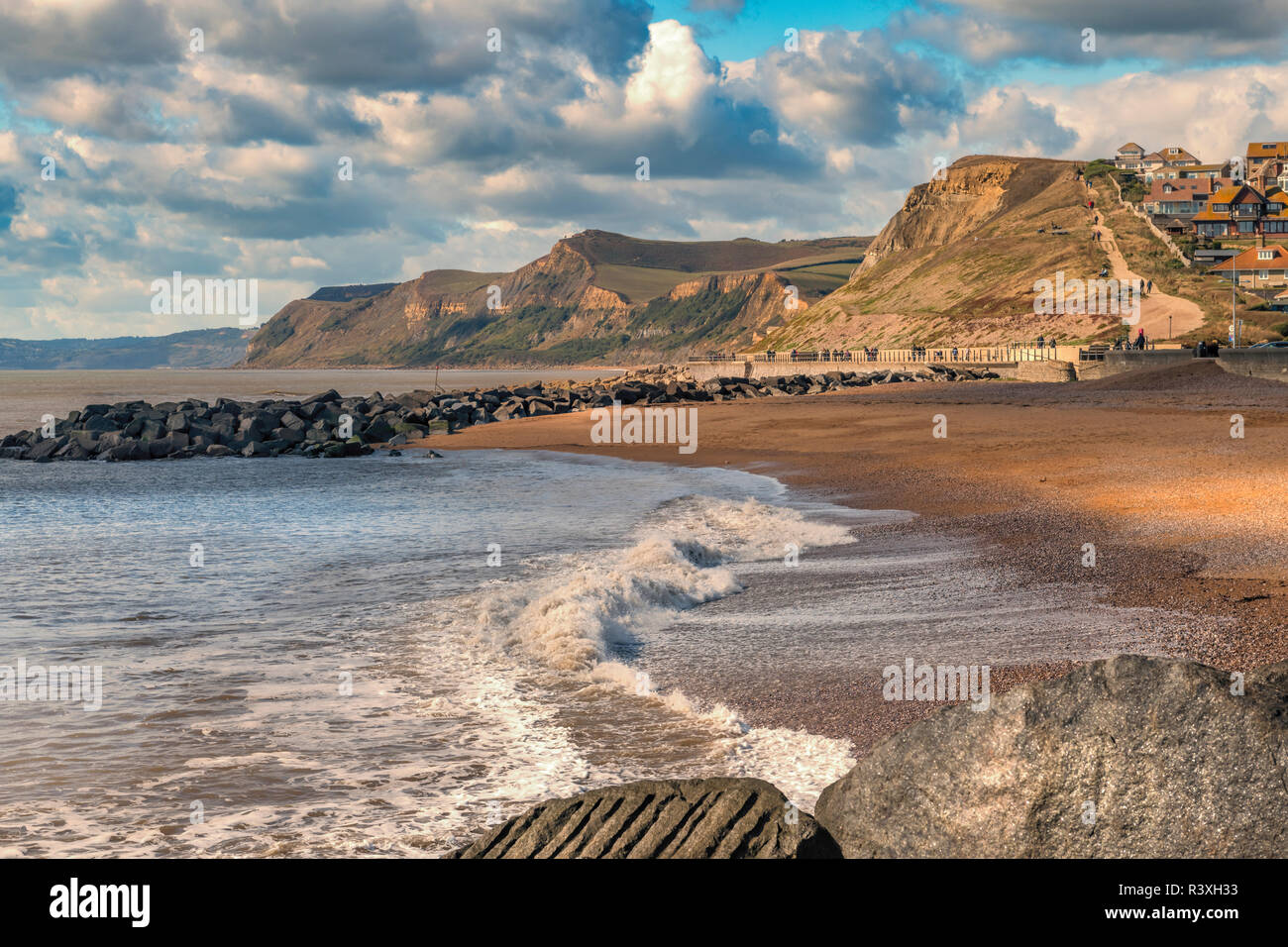 On a sunny afternoon on the Jurassic coast, a family watch the waves break onto the beautiful beach at West Bay in Dorset. Stock Photo
