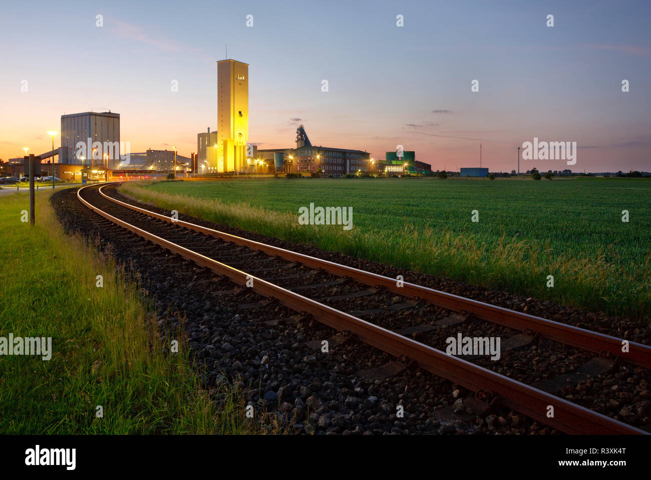 A railroad track leading to a large salt mine shortly after sunset. Stock Photo