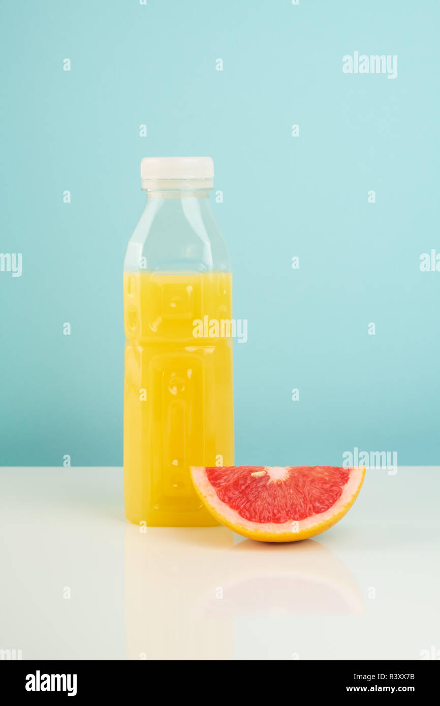 Orange drink and slice of grapefruit on white and blue background. Minimalistic image of citrus juice bottle and fruit at sparse bright environment. Stock Photo