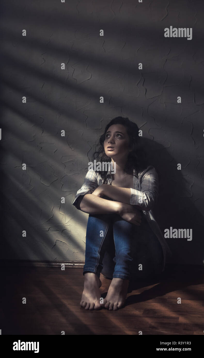 Young sad woman sitting alone on the floor in an empty room in a shadow stripe Stock Photo