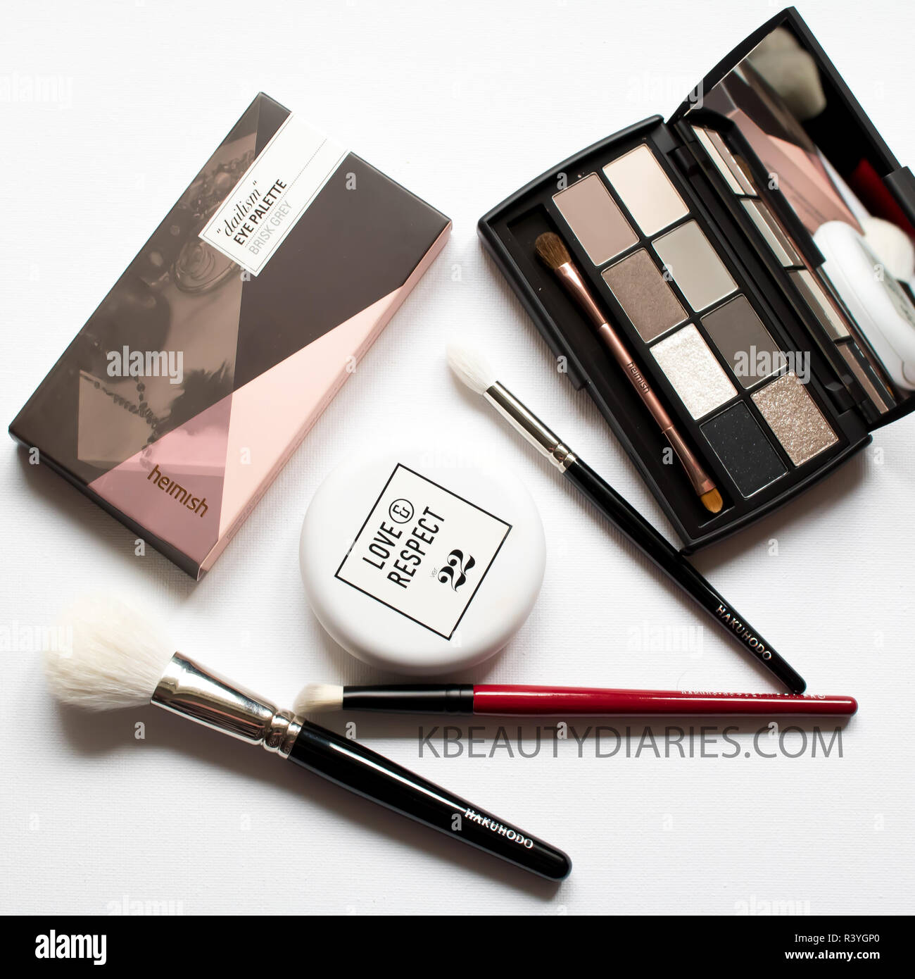 Flatlay of Make-up brushes with grey eyeshadow palette, make up brushes and cushion foundation on white background Stock Photo