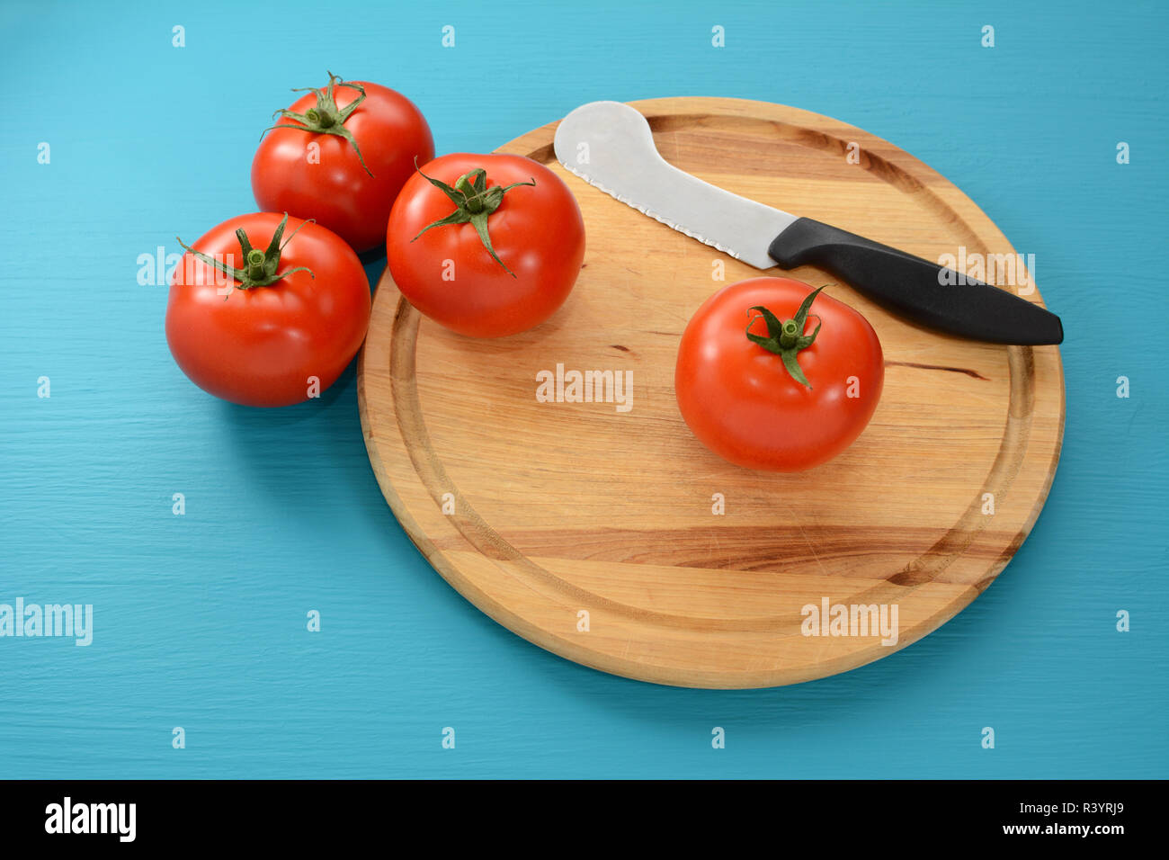 Four tomatoes on a chopping board with a knife Stock Photo - Alamy