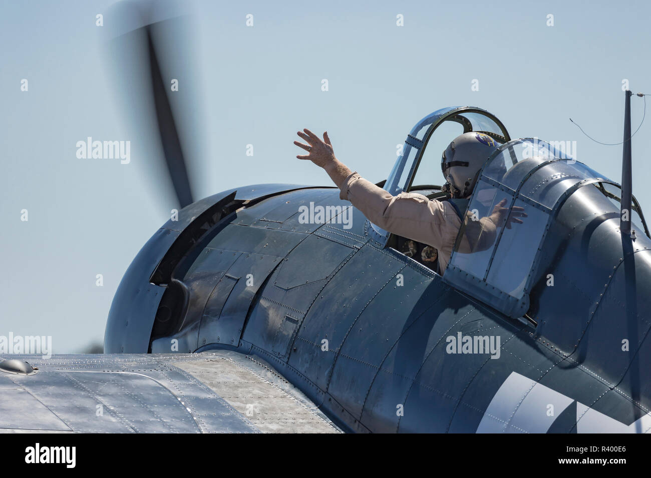 Pilot waiving from the cockpit of a Grumman F6F Hellcat fighter plane