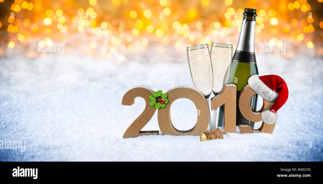 happy new year 2019 number with santa hat four leaf clover champagne bottle glass in front of golden bokeh lghts panorama snow background Stock Photo