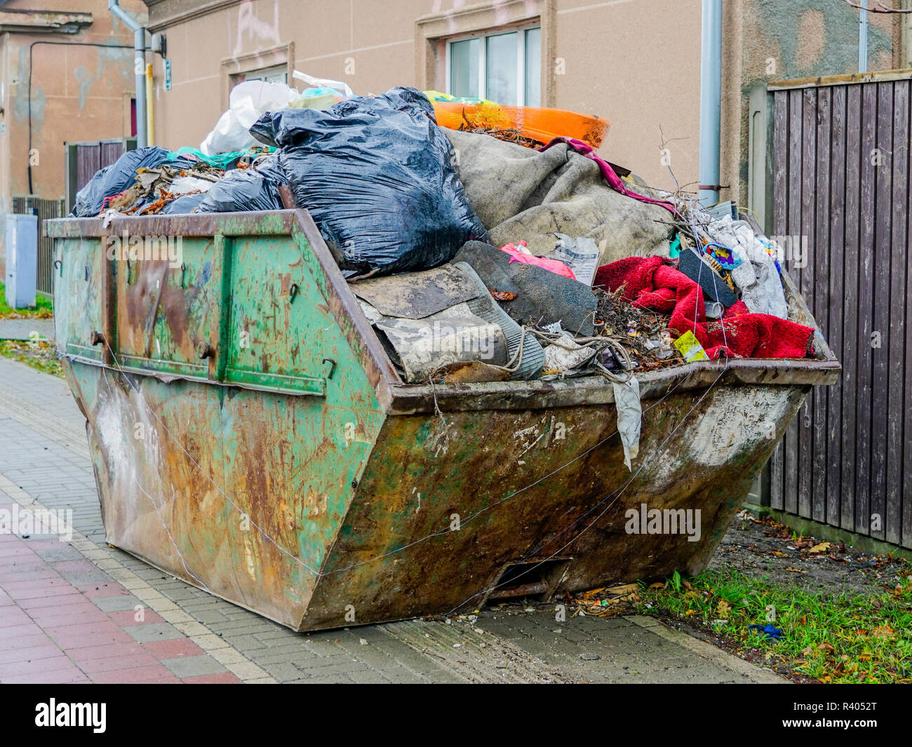 a large dirty metal waste container on the citys street, full of waste
