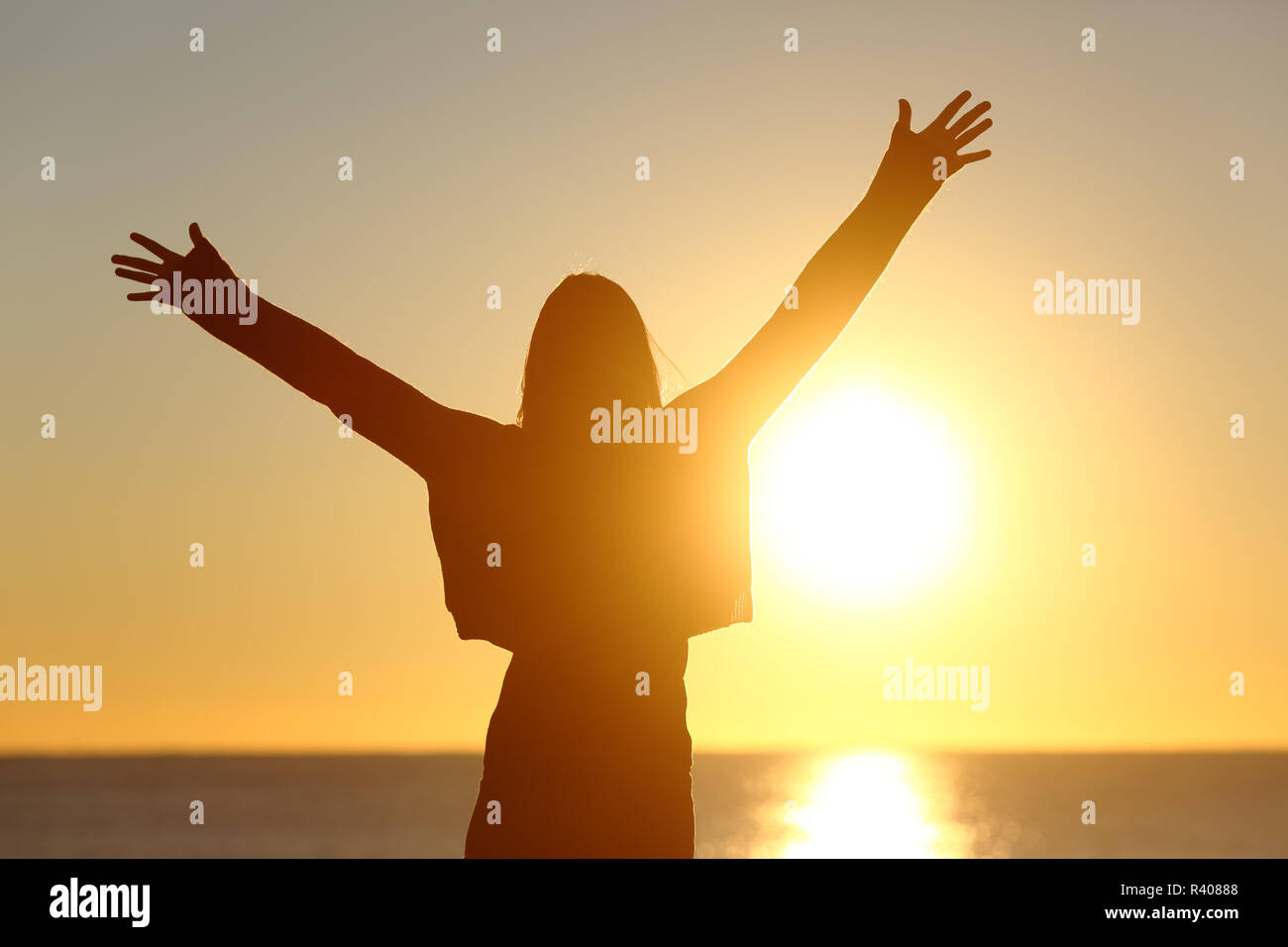 Free woman raising arms watching sun at sunrise Stock Photo