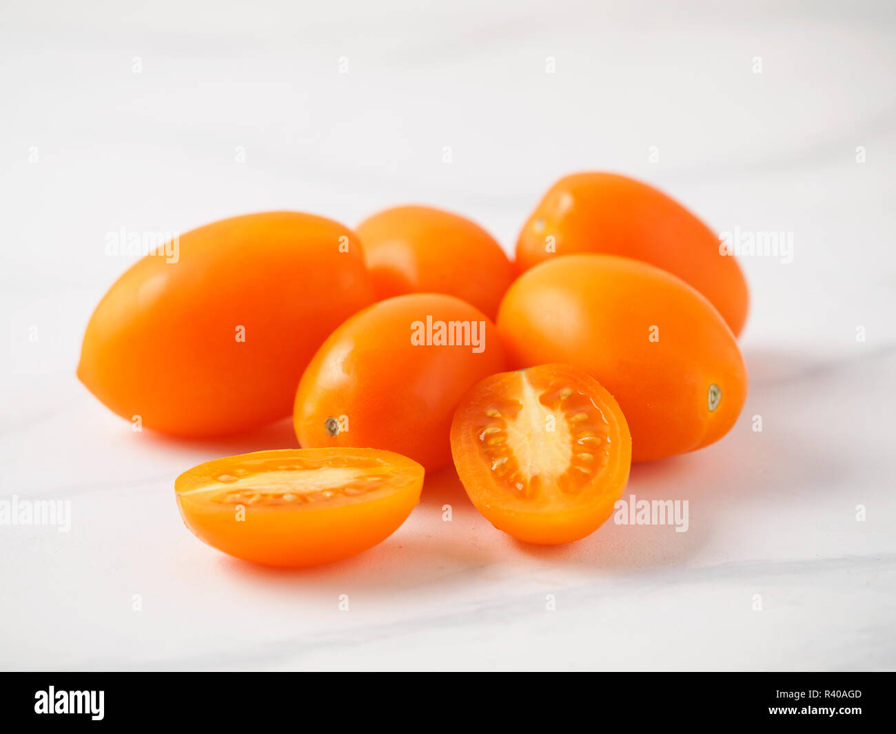 Orange tomatoes on white marble table. Yellow or orange tomatoes heap with two half sliced tomato. Copy space for text Stock Photo