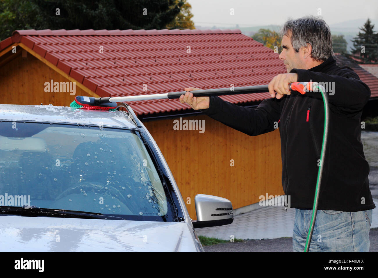 a man washes his car with water and a car wash brush Stock Photo