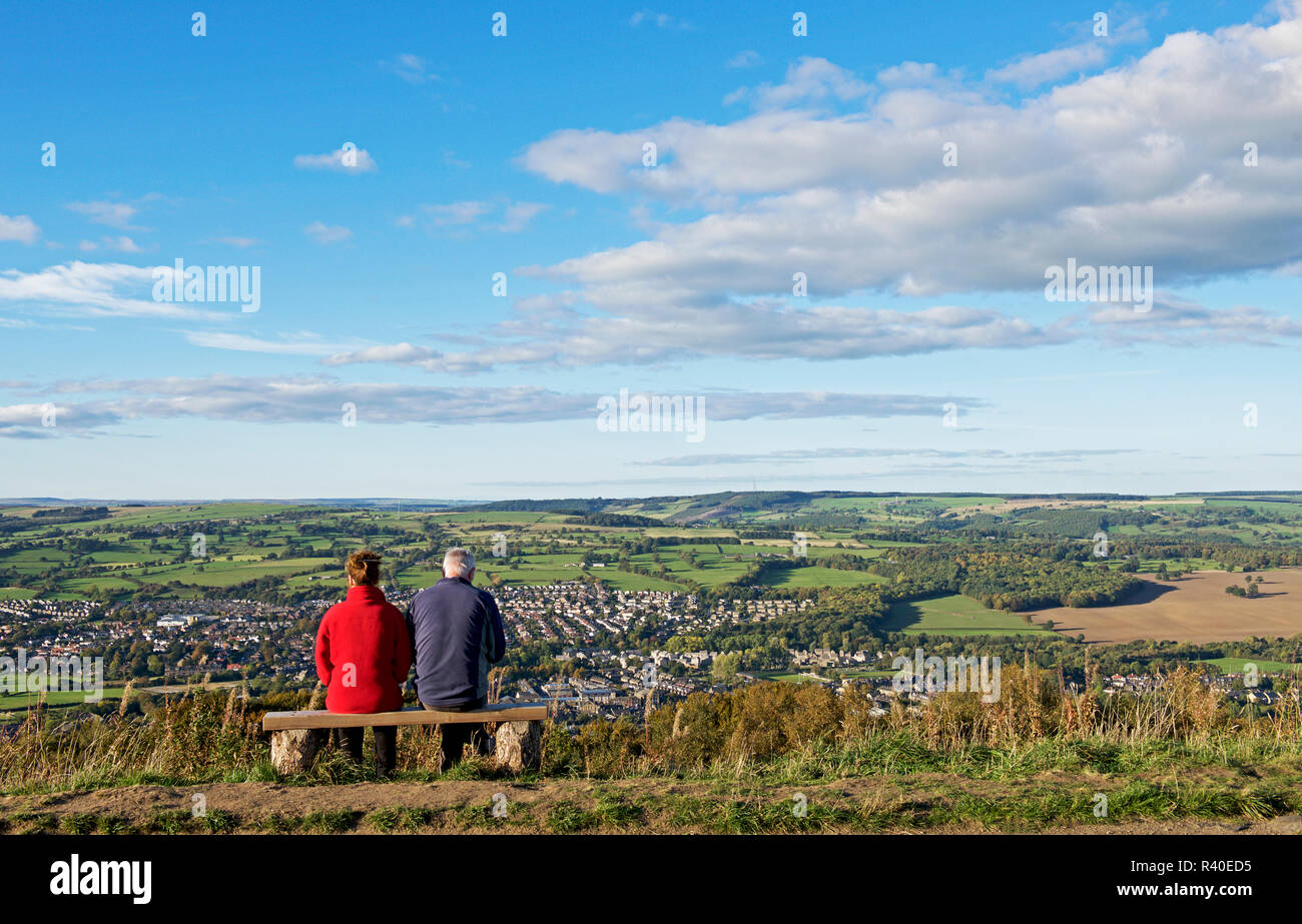 Couple sitting on bench, on the Chevin, enjoying the view over Otley and Lower Wharfedale, West Yorkshire, England UK Stock Photo