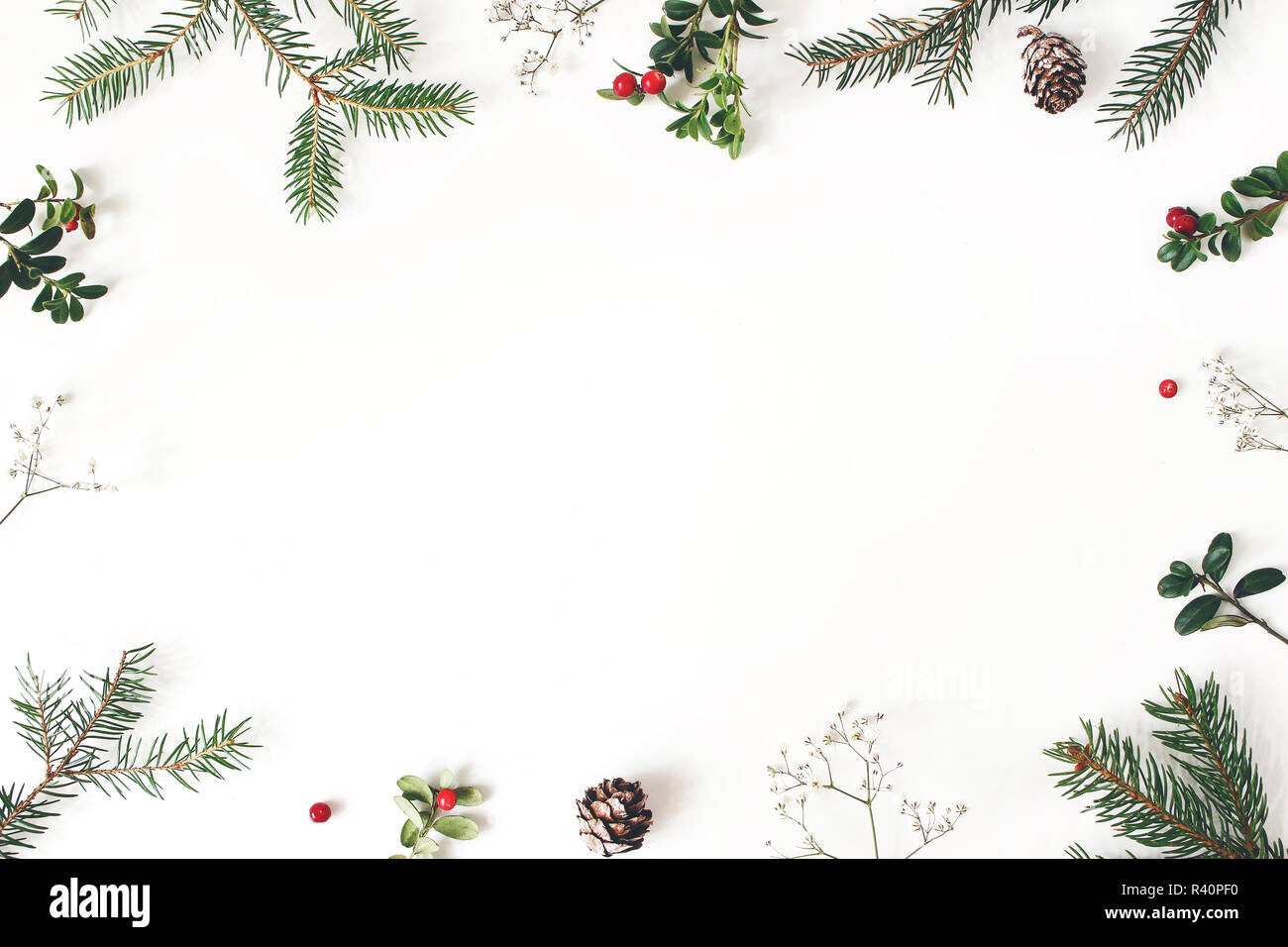 Christmas floral frame, decorative border. Winter composition of red cranberry branches, baby's breath flowers, spruce tree branches and larch cones on white table. Festive background. Flat lay, top view. Stock Photo