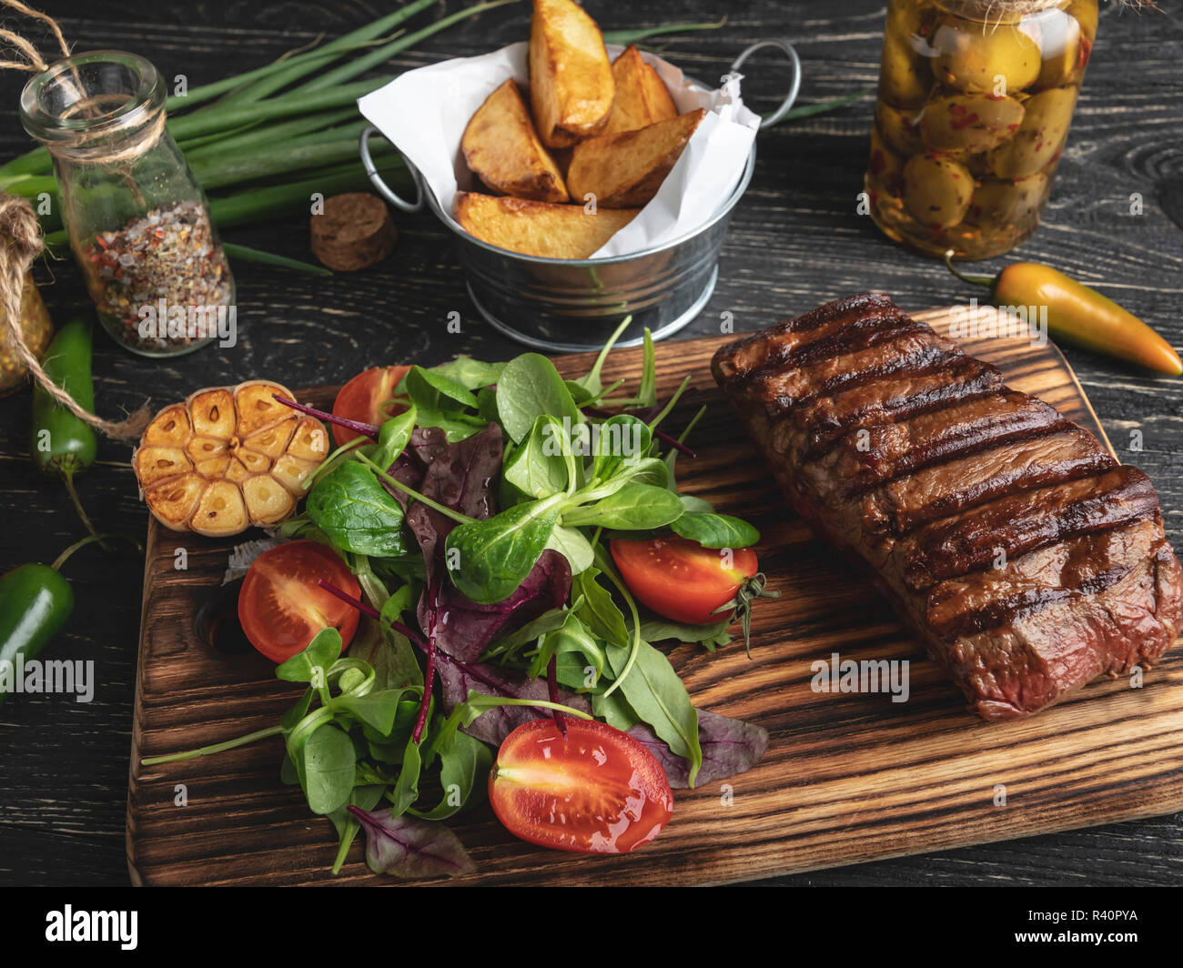 steak on the board with herbs, fried potatoes, spices on a black surface Stock Photo