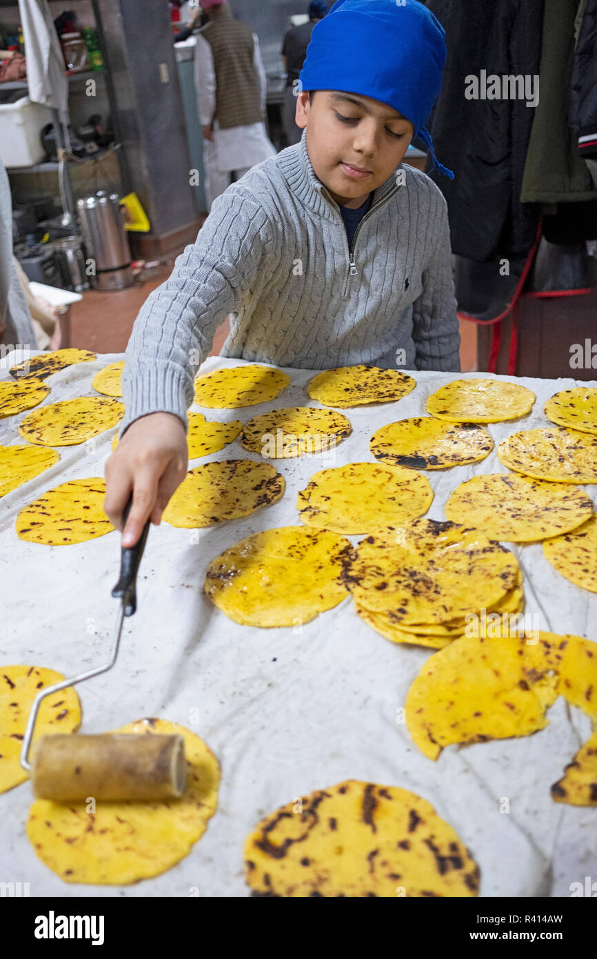 A Sikh teenager buttering roti breads in the langar of the Sikh Cultural center in Richmond Hill, Queens, New York City. Stock Photo