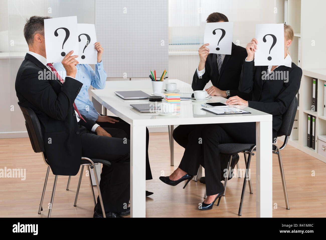 Businesspeople Hiding Faces Behind Question Mark Sign Stock Photo