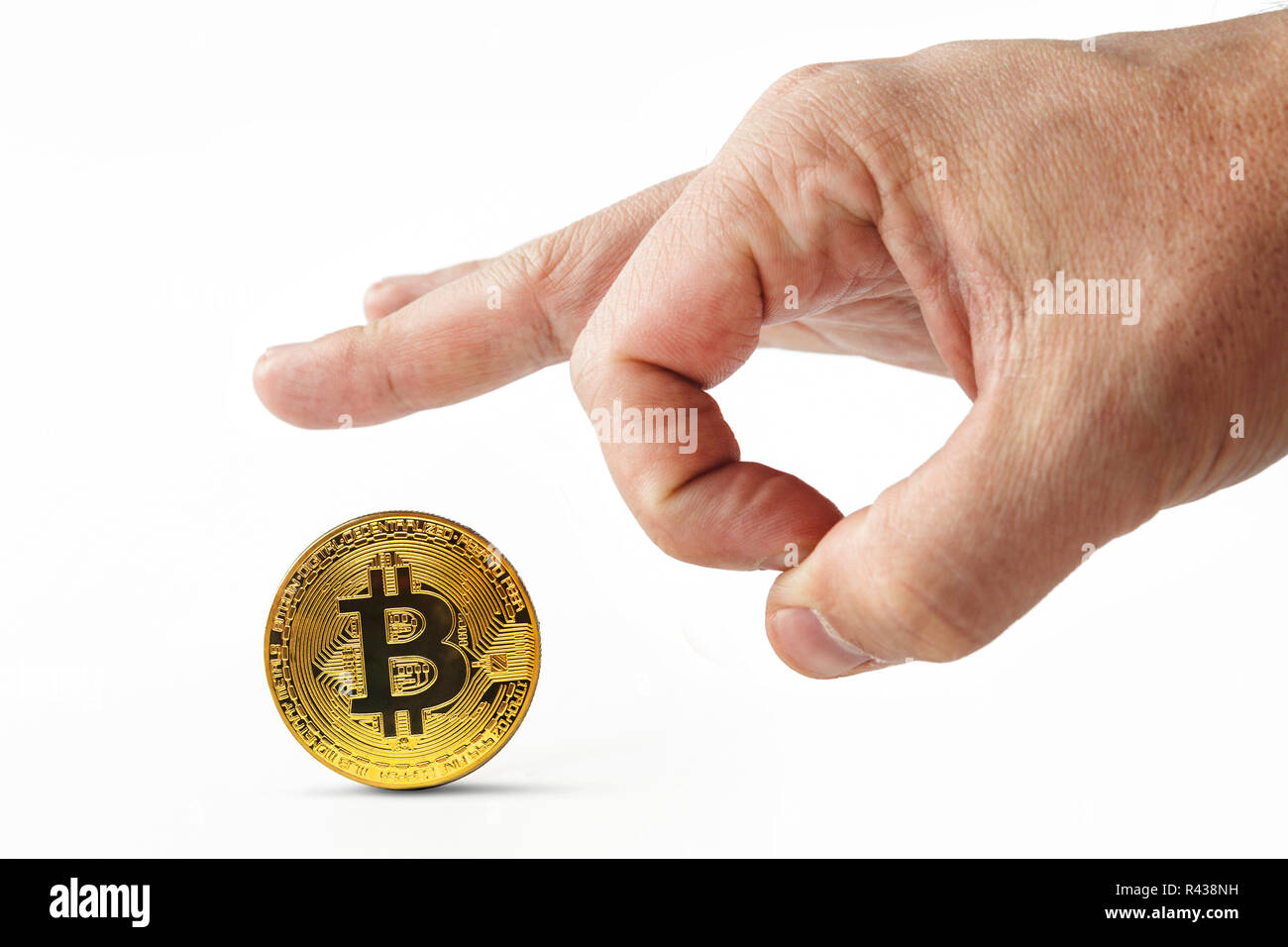 Male fingers push golden bitcoin away on a white background. Isolated man's hand throwing worthless cryptocoin away. Crash of cryptocurrency. Virtual money is depreciated. Useless bitcoins are kicked. Stock Photo